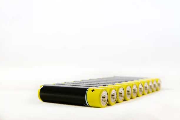 Diagonal row of yellow black AAA alkaline batteries isolated on a white background with copy-space