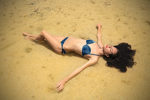 Young woman in bikini is laying on the sandy beach
