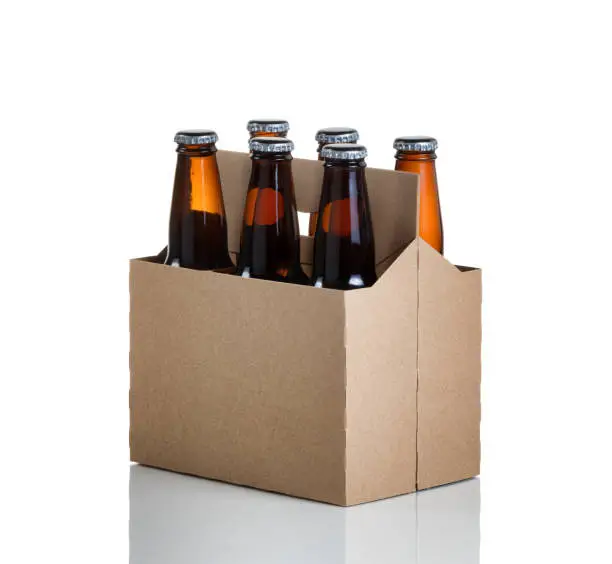 Angled view of a six pack of glass bottled beer in generic brown cardboard carrier isolated on white with reflection