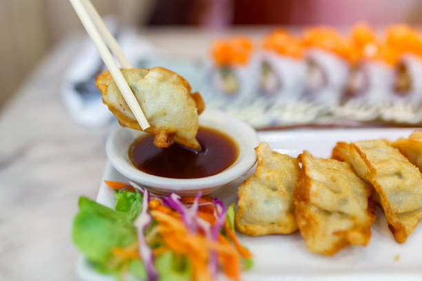 Dumpling Sauce, Close up chopsticks clamping (Japanese gyoza) dumplings sitting on a rustic wooden table in chinese restaurant.
