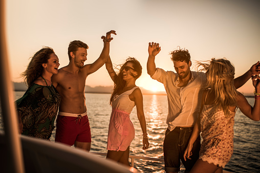 Group of happy people dancing on a boat party at sunset.
