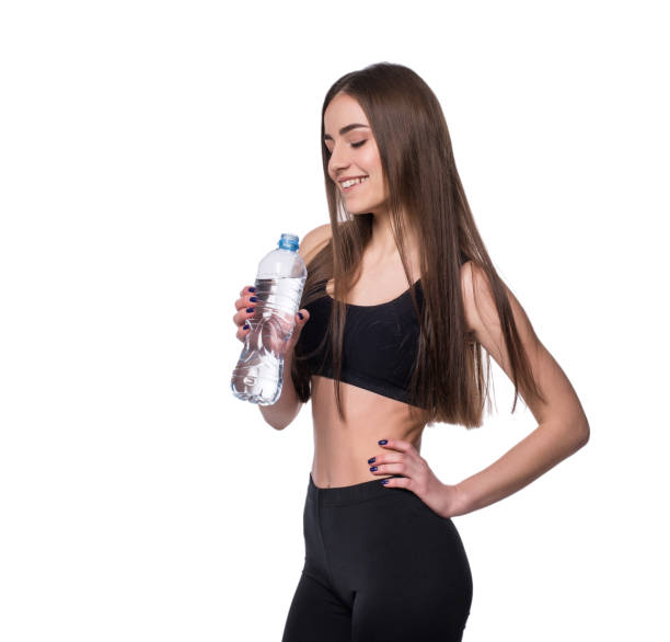 modèle positif femme fitness après entraînement tenant une bouteille d’eau pure sur fond blanc. - aerobics beautiful bottle body photos et images de collection