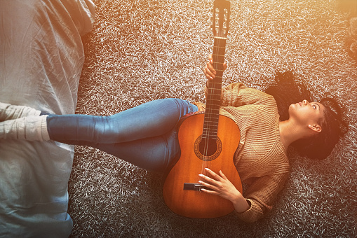 Shot of a relaxed young woman lying on the floor and playing an acoustic guitar at home