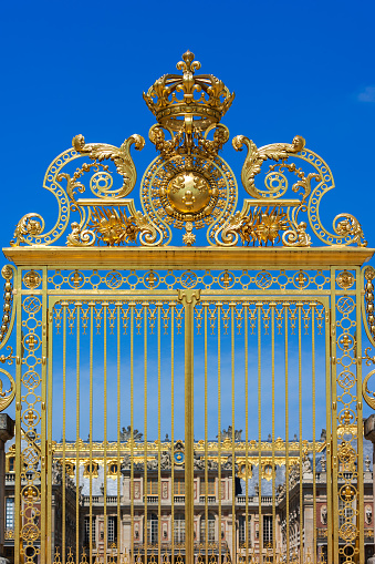 Paris, France - June 10, 2015: Golden ornate gates of the Palace of Versailles (Chateau de Versailles) over blue sky. Paris, France