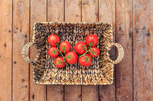 Basket with fresh red cherry tomatoes on wooden table, view directly above.