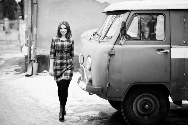 istock Young red haired girl posed on checkered dress background old retro cyan minivan. 652932242