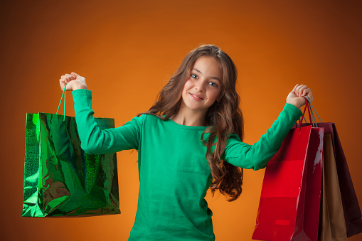 The cute cheerful little girl with shopping bags on orange background