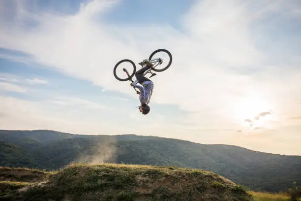 Mountain bike cyclist exercising in nature and practicing backflip against the sky.
