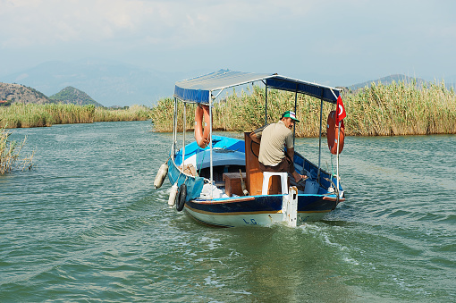 Mugla, Turkey - August 13, 2009: Unidentified man rides tourist boat at the Dalyan river in Mugla, Turkey.