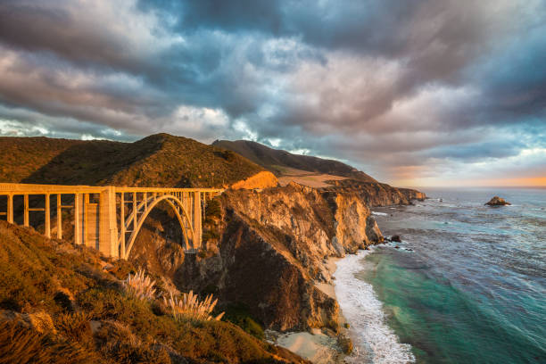 Bixby Bridge along Highway 1 at sunset, Big Sur, California, USA Scenic panoramic view of historic Bixby Creek Bridge along world famous Highway 1 in beautiful golden evening light at sunset with dramatic cloudscape in summer, Monterey County, California, USA Bixby Creek stock pictures, royalty-free photos & images