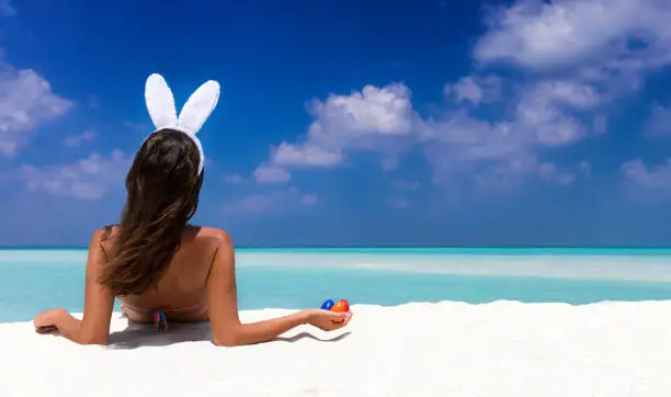 Photo of Woman with bunny ears and colorful easter eggs on a beach