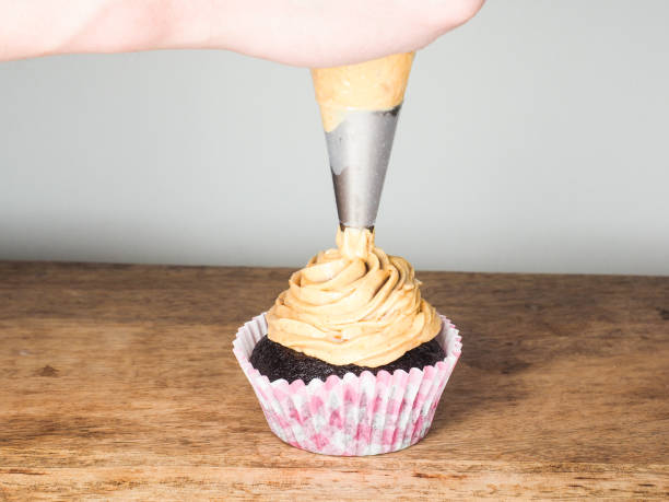 istock Professional cake baker applying frosting onto chocolate cupcake 653047118