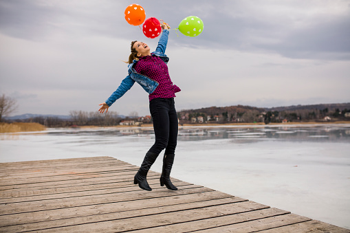 Happy woman jumping with balloons at dock