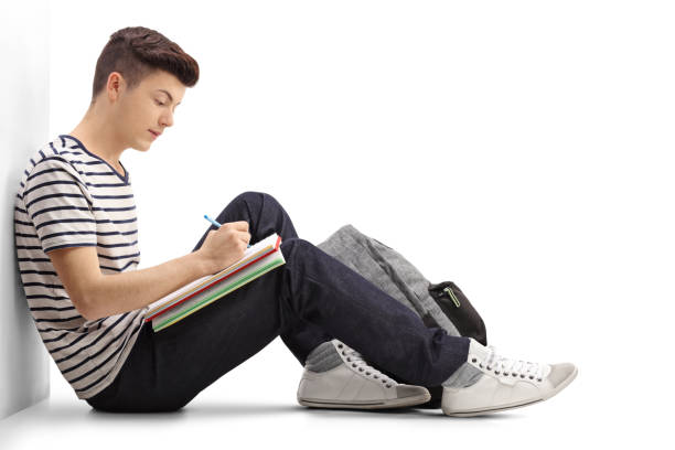 Teen student writing in a notebook Teen student writing in a notebook and leaning against a wall isolated on white background teenagers only photos stock pictures, royalty-free photos & images