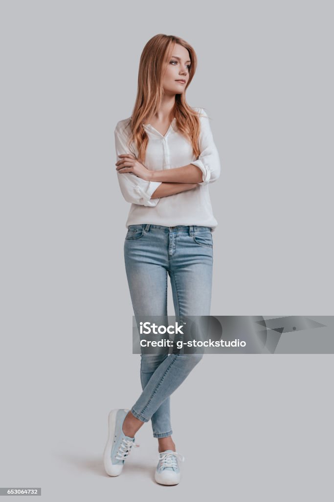 Thinking about? Full length of beautiful young woman in casual wear keeping arms crossed and looking away while standing against grey background Women Stock Photo