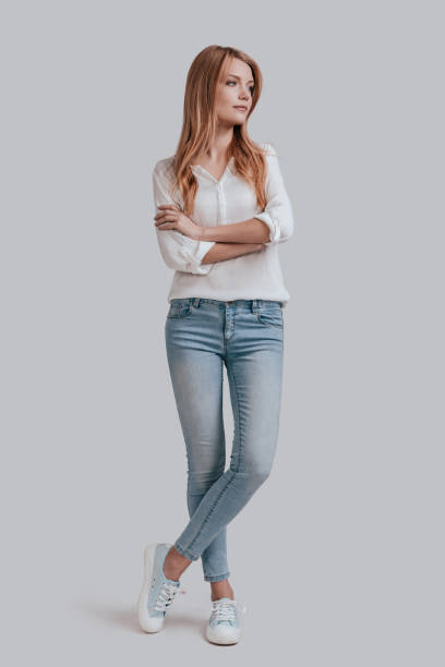 Thinking about? Full length of beautiful young woman in casual wear keeping arms crossed and looking away while standing against grey background women young women standing full length stock pictures, royalty-free photos & images