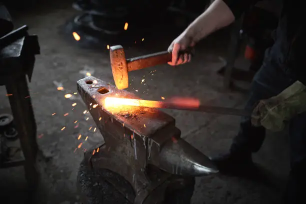 Blacksmith hitting red-hot metal with hammer to change shape