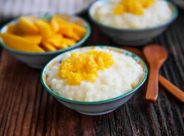 Rice milk pudding with mango jam in bowls with wooden spoons, homemade dessert