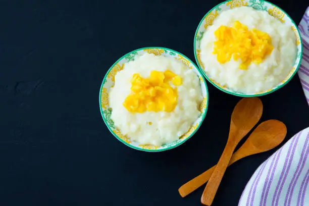 Rice milk pudding with mango jam in bowls with wooden spoons, homemade dessert