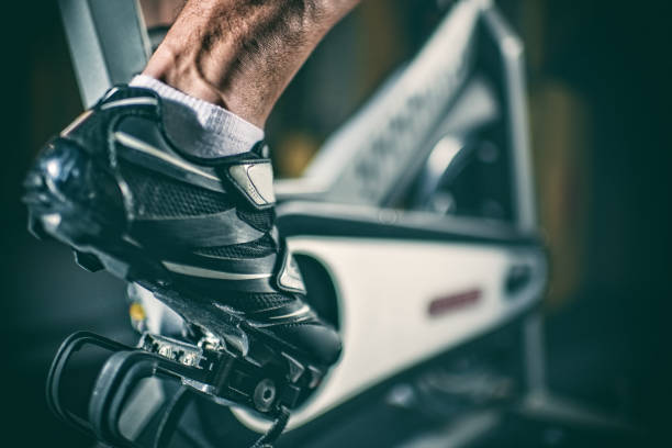Foot on stationary bicycle Close up view of sports shoe placed on the pedal of stationary bicycle. spin bike stock pictures, royalty-free photos & images
