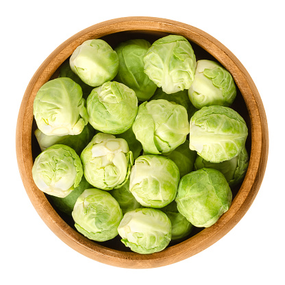 Brussels sprouts in wooden bowl. The leafy green vegetables look like miniature cabbages. Raw edible buds, member of Gemmifera group. Isolated macro food photo close up from above on white background.