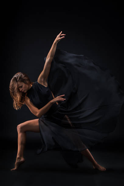 istock Young beautiful dancer in beige dress dancing on black background 653117174