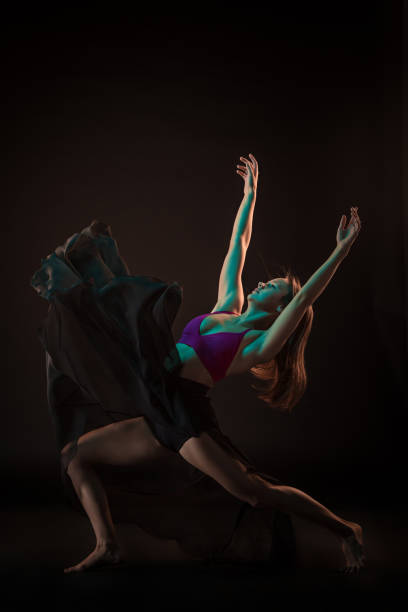 istock Young beautiful dancer in beige dress dancing on black background 653120246