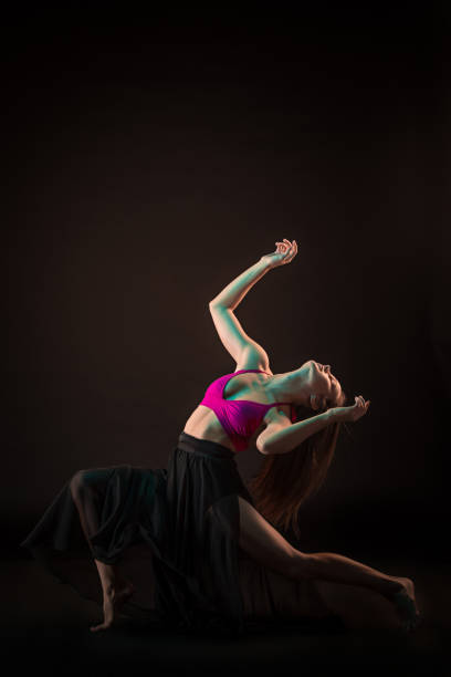 istock Young beautiful dancer in beige dress dancing on black background 653120314