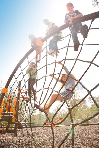 Multi-ethnic elementary school children playing on playground at park. Multi-ethnic group of elementary age school children playing on a school or park playground in spring or summer season.  They enjoy climbing on the rope equipment. group of people people recreational pursuit climbing stock pictures, royalty-free photos & images