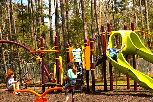 Multi-ethnic group of elementary age school children playing on a school or park playground in spring or summer season.