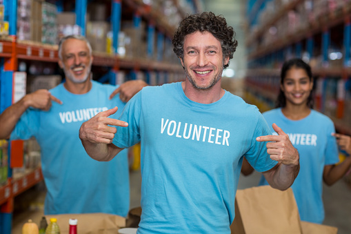 Portrait of volunteers pointing at t-shirt in warehouse
