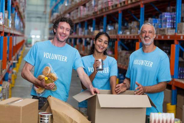 istock Three volunteers packing eatables in cardboard box 653155970