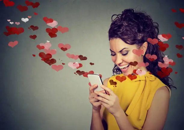 Photo of Beautiful happy woman sending love text message on mobile phone with red hearts