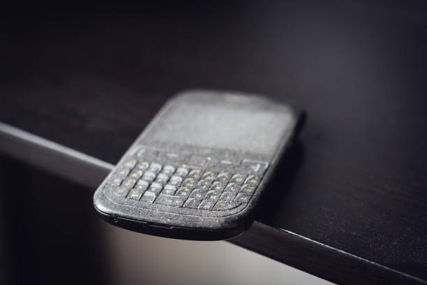 side view close up of old black smartphone mobile with qwerty keyboard covered in dust left on a black wooden shelf