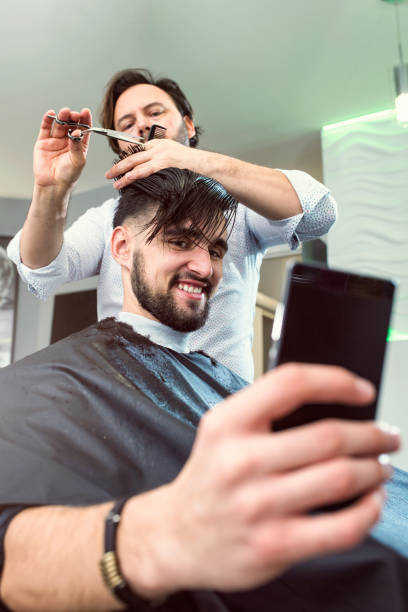 istock Men in a Barber Shop Using Smart Phone While Having Haircut 653184542