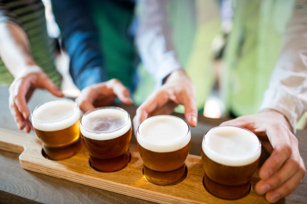 Midsection of friends reaching towards beer sampler at bar counter