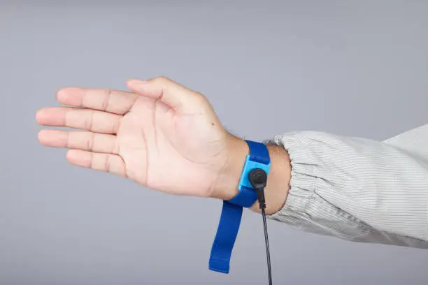 Photo of Ground bracelet on man hand wearing ESD cloth gray background. Antistatic (ESD) wrist strap or ground bracelet is an antistatic device used to safely ground a person working on electronic equipment.