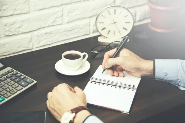 istock Man's hand holding a pen on paper notebook on table 653211852