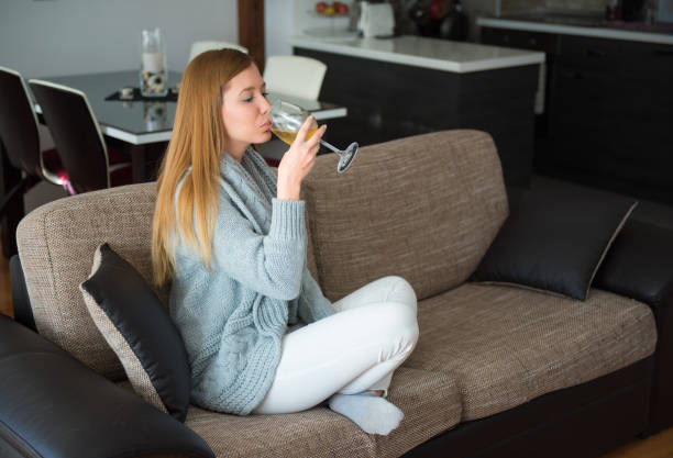istock Single woman sitting on sofa and drinking white wine 653230356