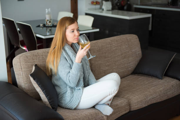 istock Single woman sitting on sofa and drinking white wine 653230580