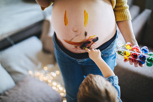Little boy painting his pregnant mother with finger paint