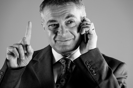 Businessman gesturing with his finger as he listens to a conversation on his mobile phone, close up cropped greyscale image