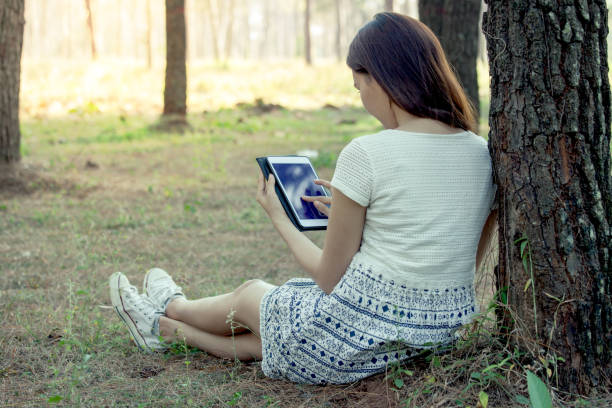 istock Young asian woman using tablet in the park 653270778
