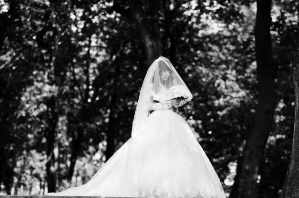 istock Gorgeous curly brunette bride with wedding bouquet on hands posed on park. 653313894