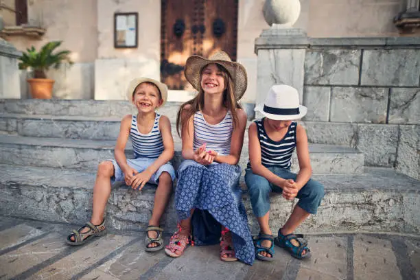 Sister and two brothers having fun visiting the beautiful Majorcan town of Alcudia. Kids are resting on stairs, having fun and laughing.
