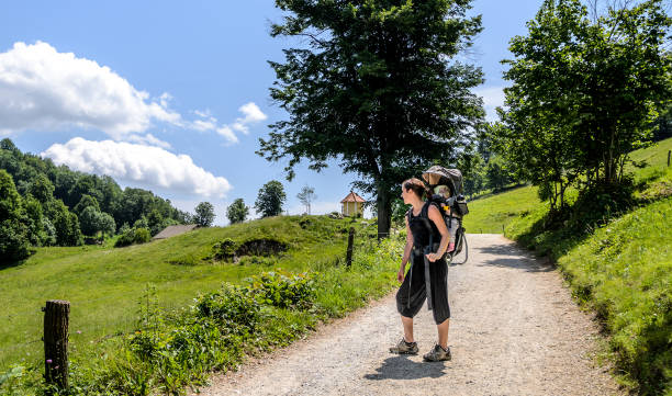 Mother with baby in backpack carrier is hiking in mountains.