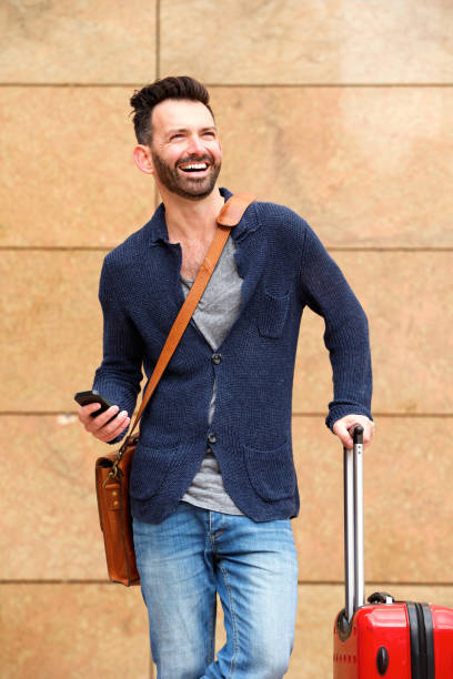 istock Smiling mature man standing outdoors with bag and mobile phone 653355200