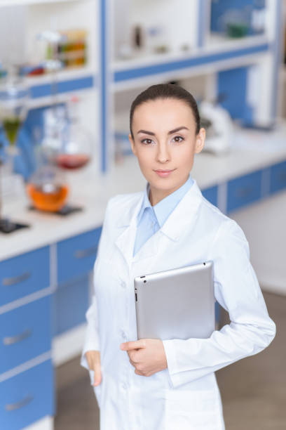 istock Young confident woman scientist in lab coat holding digital tablet and looking at camera 653364362