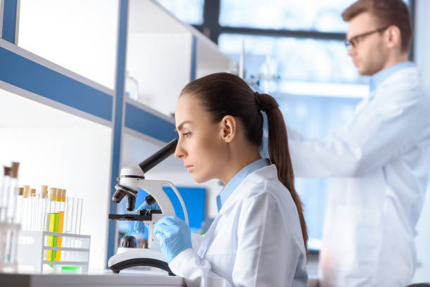 istock side view of scientist looking through microscope near colleague in laboratory 653364628