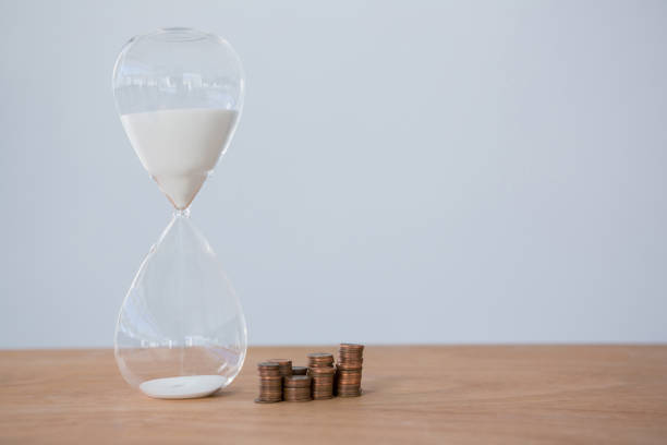 istock Hourglass and stacks of coins on table 653382616